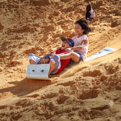 Sandboarder gliding down the golden dunes of Mũi Né at sunset Vietnam